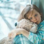 girl in blue white and red plaid shirt hugging brown teddy bear