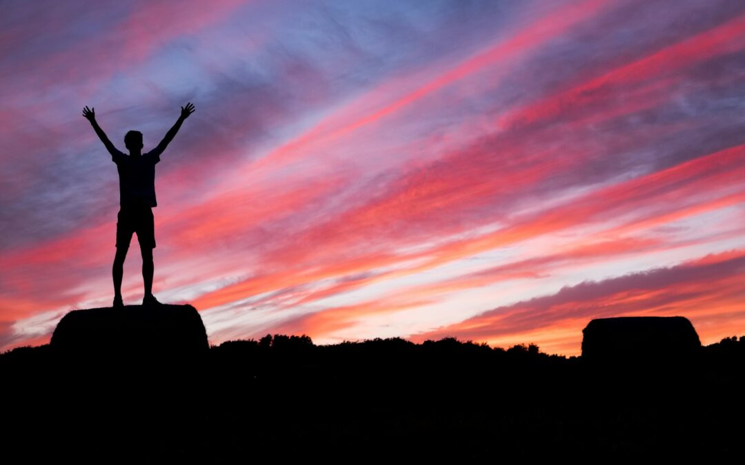 silhouette of man standing on high ground under red and blue skies