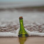 green glass bottle with cork lid on shore