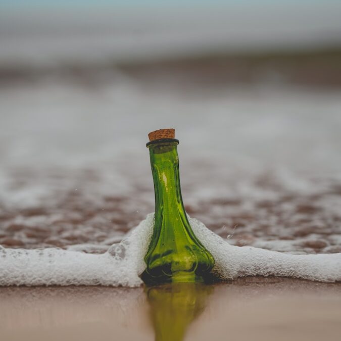 green glass bottle with cork lid on shore