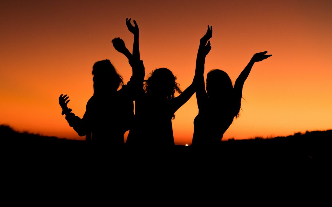 silhouette of three woman with hands on the air while dancing during sunset
